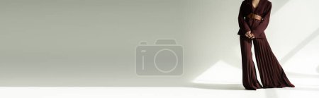 Foto de Vista recortada del modelo en pantalones palazzo y chaqueta con cinturón de cuero sobre fondo gris con iluminación, pancarta - Imagen libre de derechos