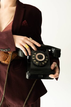 partial view of stylish woman in blazer and finger rings holding vintage telephone isolated on grey