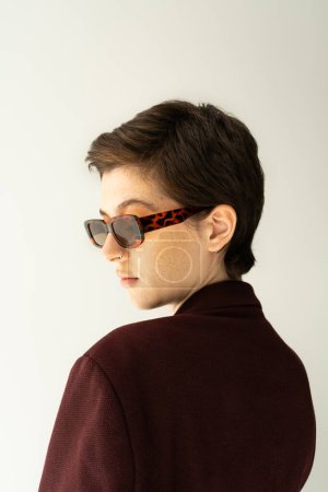 Foto de Retrato de mujer morena con pelo corto posando en elegantes gafas de sol aisladas en gris - Imagen libre de derechos