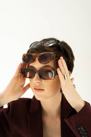  Porträt einer trendigen Frau mit verschiedenen modischen Sonnenbrillen isoliert auf grau