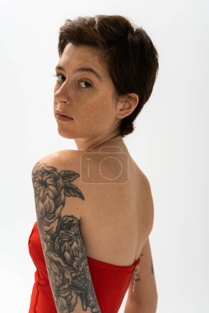 Photo for Portrait of young woman with tattoo and freckles looking at camera isolated on grey - Royalty Free Image