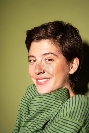 portrait of joyful woman with freckles and short brunette hair looking at camera on green background