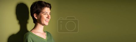 carefree brunette woman in striped jumper looking away on green background with shadow, banner