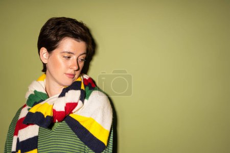 nachdenkliche brünette Frau im gestreiften bunten Schal auf grünem Hintergrund