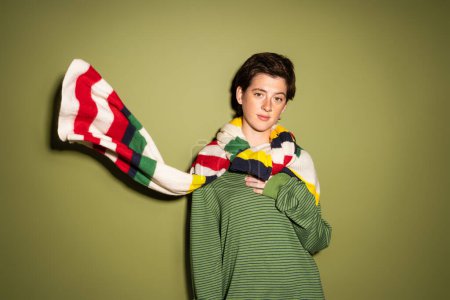 young brunette woman in spring pullover and striped multicolored scarf waving on wind on green background