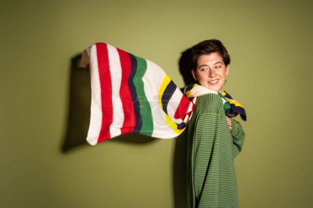 fröhliche Frau blickt auf gestreiften bunten Schal, der im Wind auf grünem Hintergrund weht
