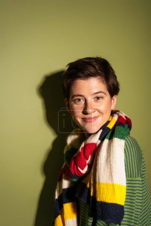 Photo for Portrait of carefree woman wearing trendy scarf and smiling at camera on green background with shadow - Royalty Free Image