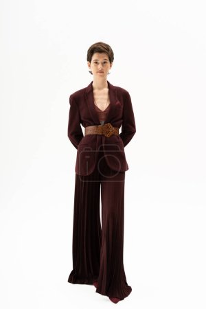 full length of elegant woman in blazer and wide pants standing on white background