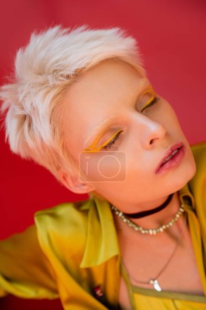 Porträt einer blonden Albino-Frau mit hellem Eyeliner und geschlossenen Augen auf karminrosa 