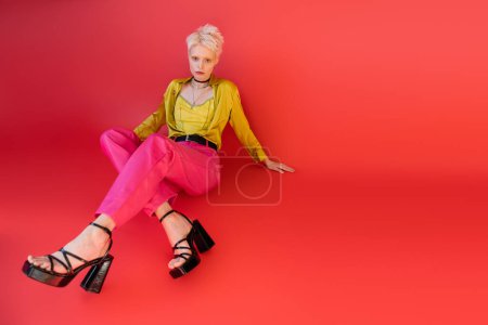 full length of blonde model in trendy clothes and heeled sandals posing on carmine pink background 