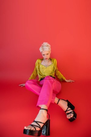 Foto de Longitud completa de modelo joven en ropa de moda y sandalias de tacón posando sobre fondo rosa carmín - Imagen libre de derechos