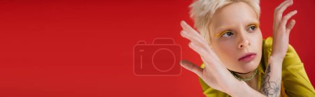 Foto de Mujer albina tatuada con delineador de ojos amarillo mirando hacia otro lado mientras posa en carmín rosa, pancarta - Imagen libre de derechos