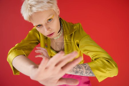 overhead view of blonde albino woman with tattoo looking at camera while posing on carmine pink background  