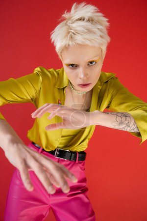 high angle view of albino woman with tattoo looking at camera while posing on carmine pink 