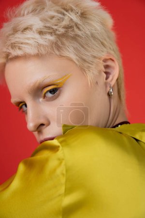 Porträt einer blonden Albino-Frau mit hellem Eyeliner, die in die Kamera auf karminrosa blickt 