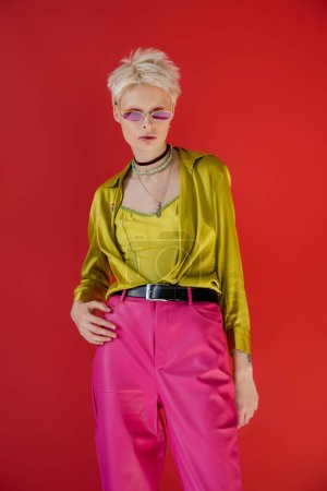 tätowiertes Albino-Model in stylischem Outfit und Sonnenbrille posiert auf karminrosa  