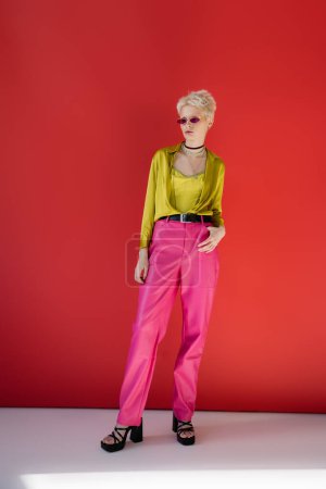 full length of albino model in trendy outfit and sunglasses posing on carmine pink 