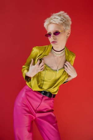 tätowiertes Albino-Model in hellem Outfit und trendiger Sonnenbrille posiert auf karminrosa 