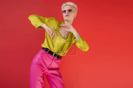 Photo for Albino model with tattoo posing in stylish blouse and trendy sunglasses on carmine pink background - Royalty Free Image