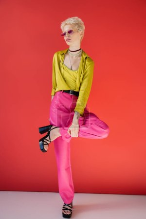 full length of albino model with tattooed hand posing in stylish heeled sandals on carmine pink 