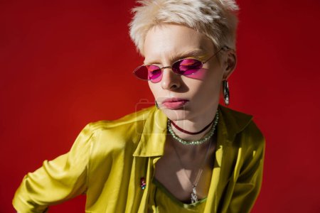 Téléchargez les photos : Lumière du soleil sur le visage du modèle albinos dans des lunettes de soleil élégantes sur fond rose carmin - en image libre de droit