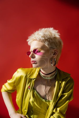 sunlight on face of albino model in stylish sunglasses and blouse posing on carmine pink background 