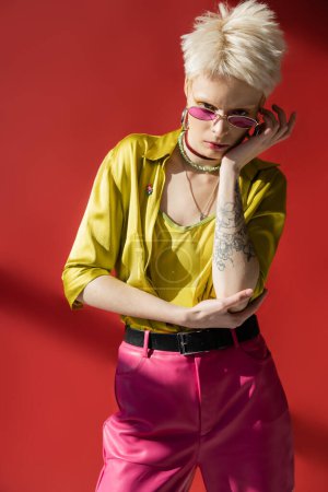 sunlight on face of albino woman with tattoo posing in stylish sunglasses on carmine pink 
