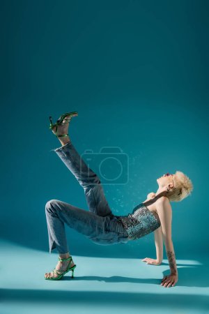 Photo for Full length of tattooed albino model in pink sunglasses posing with raised leg on blue - Royalty Free Image