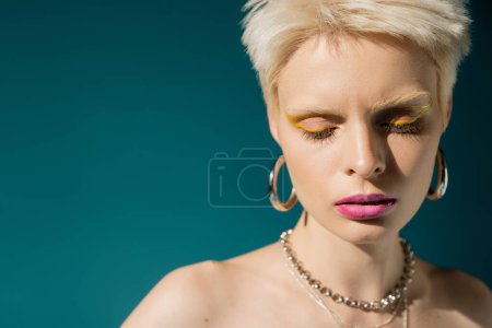 Foto de Retrato de mujer albina rubia con maquillaje de moda posando en joyería sobre fondo azul - Imagen libre de derechos