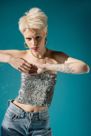 tätowiertes Albino-Model im modischen Outfit blickt in die Kamera auf blauem Hintergrund 