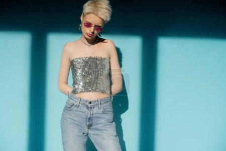 sunlight on body of albino woman in pink sunglasses and shiny top with sequins on blue background 
