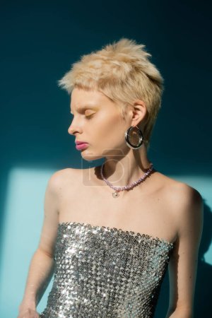sunlight on face of albino woman in shiny top with sequins posing on blue 