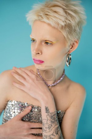 Photo for Blonde albino woman in shiny top with sequins posing on blue background - Royalty Free Image