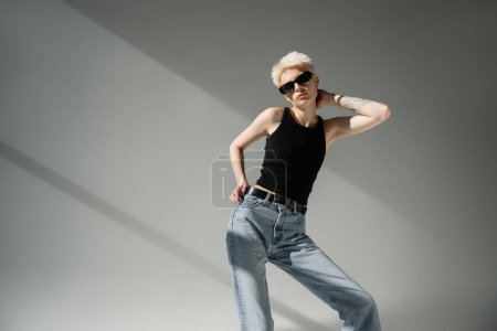 Photo for Tattooed woman in black sunglasses and tank top posing on grey background - Royalty Free Image