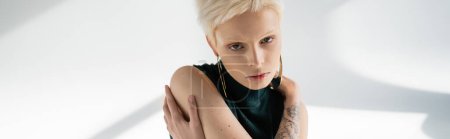 Téléchargez les photos : Jeune femme albinos avec tatouage à la main s'étreignant sur fond gris avec des ombres, bannière - en image libre de droit