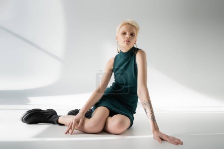 full length of pretty albino woman in tight dress and boots posing on grey background with shadows 