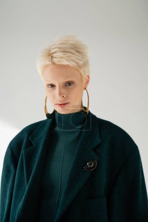 portrait of young albino woman in green dress and coat posing on grey background 