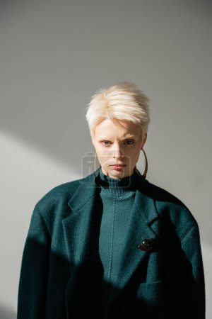 young albino woman with fair-skin posing in green dress and coat on grey background 