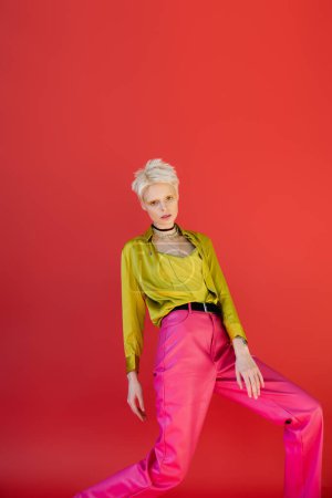 blonde woman with bright eyeliner posing in trendy outfit on carmine pink background