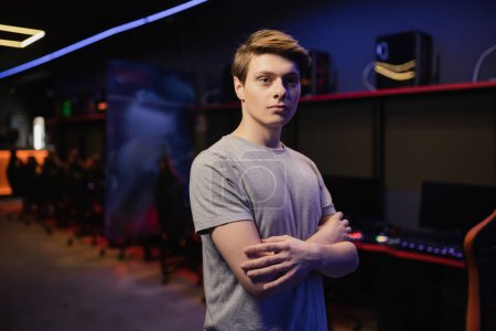 Young gamer crossing arms and looking at camera in gaming club 