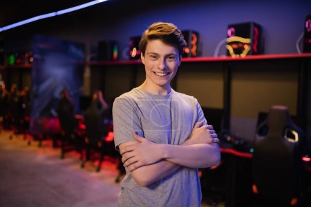 Young gamer crossing arms and smiling at camera in gaming club 