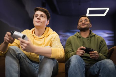 Photo for KYIV, UKRAINE - FEBRUARY 13, 2023: Low angle view of young man playing video game with blurred indian friend in gaming club - Royalty Free Image