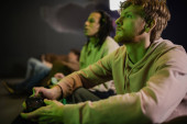 KYIV, UKRAINE - FEBRUARY 13, 2023: Young man playing video game with blurred multiracial friend in gaming club  Longsleeve T-shirt #650688170