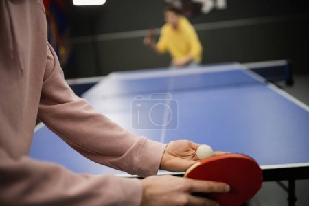 Ausgeschnittene Ansicht eines Mannes, der mit verschwommenem Freund in Spielclub Tischtennis spielt 