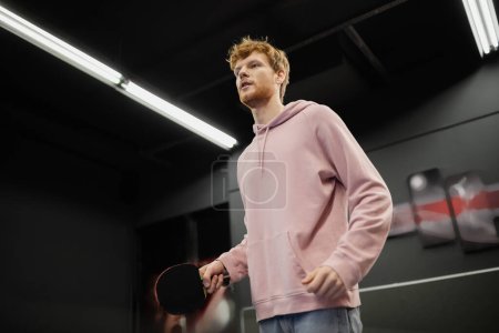 Low angle view of redhead man holding tennis racket in gaming club 