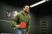 Cheerful indian man with racket playing table tennis in gaming club  magic mug #650688538