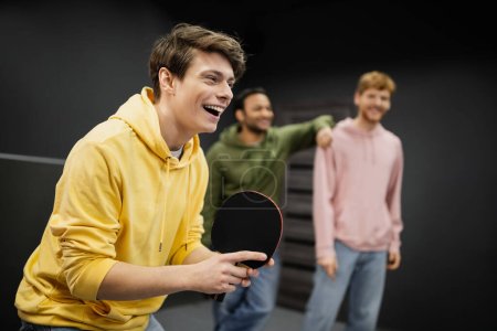 Cheerful man playing table tennis near blurred friends in gaming club 
