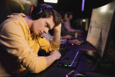 Foto de Hombre molesto en los auriculares sentados cerca de la computadora en el club cibernético - Imagen libre de derechos