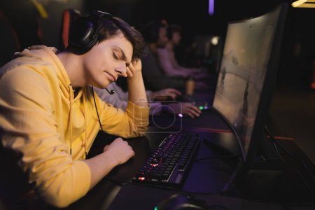 Displeased gamer in headphones sitting near computer in gaming club 