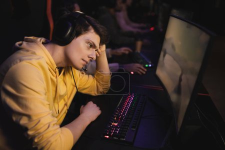 Trauriger Mann mit Kopfhörern blickt in Cyber-Club auf Computer 